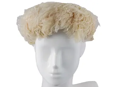 Pillbox shaped hat covered in white feathers. Interior is off-white lace. An Evelyn Model label attributes this hat to Parisian milliner Evelyn Varon. 