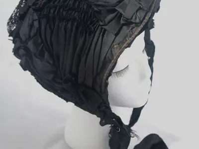 Black silk bonnet styled with ribbon, lace, and dark purple feathers.